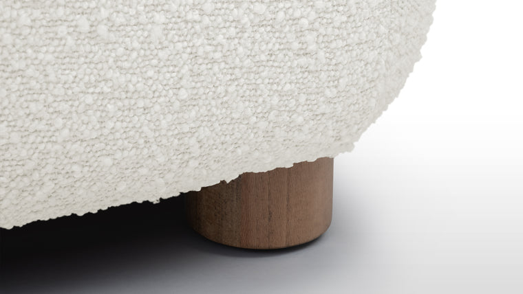 Textured Comfort | Selected in a warm white shade, the boucle upholstery features a looped texture that offers a cushioned feel, while the footstool's sturdy wooden legs provide a contrasting yet complementary foundation.
